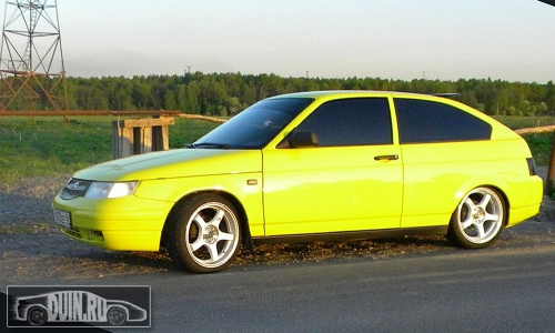 ВАЗ 2112 купе (Lada 112) цвет Акапулько 243 ярко-жёлтый, вид сбоку, на белой ковке, тонировка, большие диски
